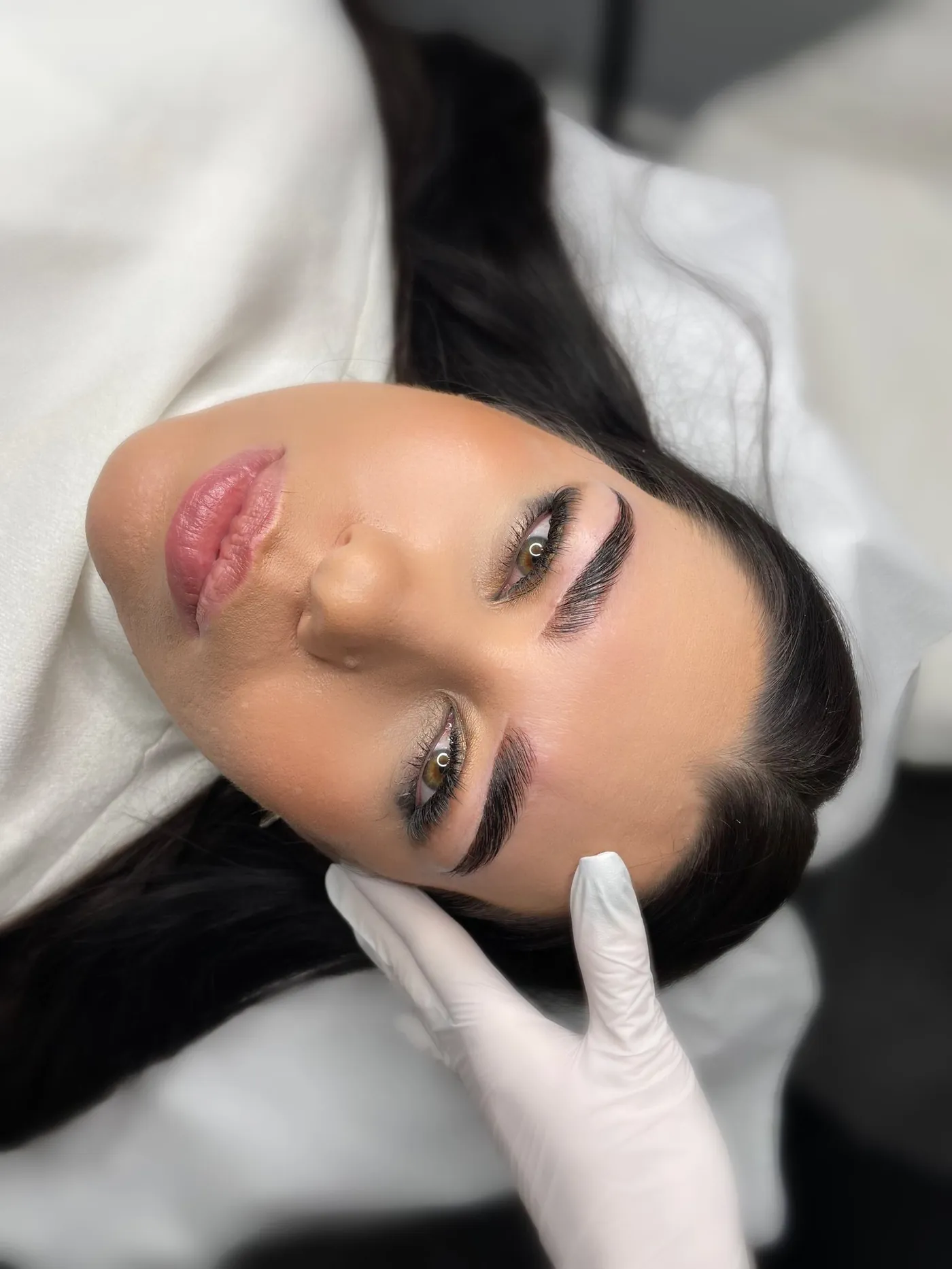 Gloved brow artist checking a client's soft ombre brows